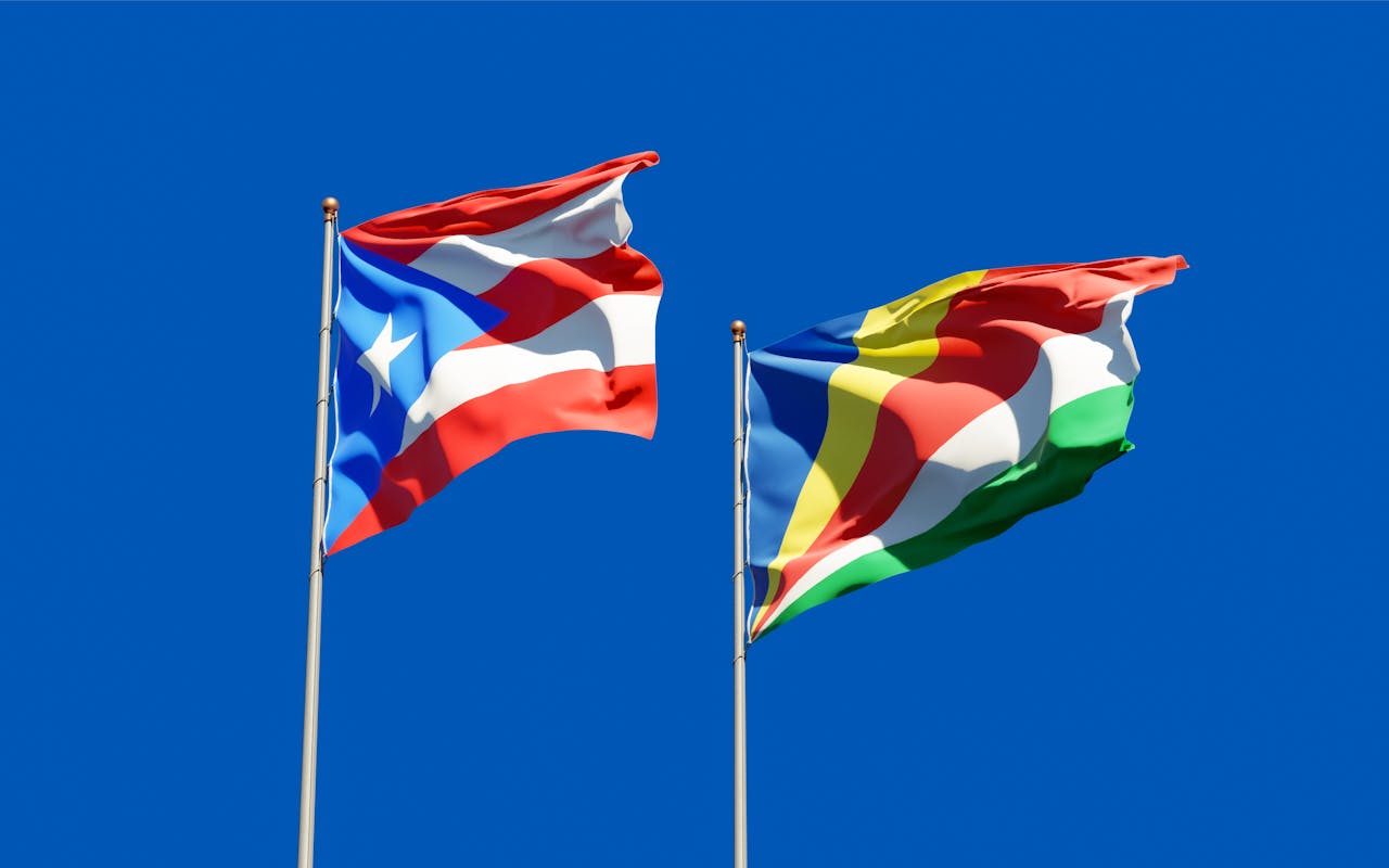 Waving flags of Puerto Rico and Seychelles against a clear blue sky.